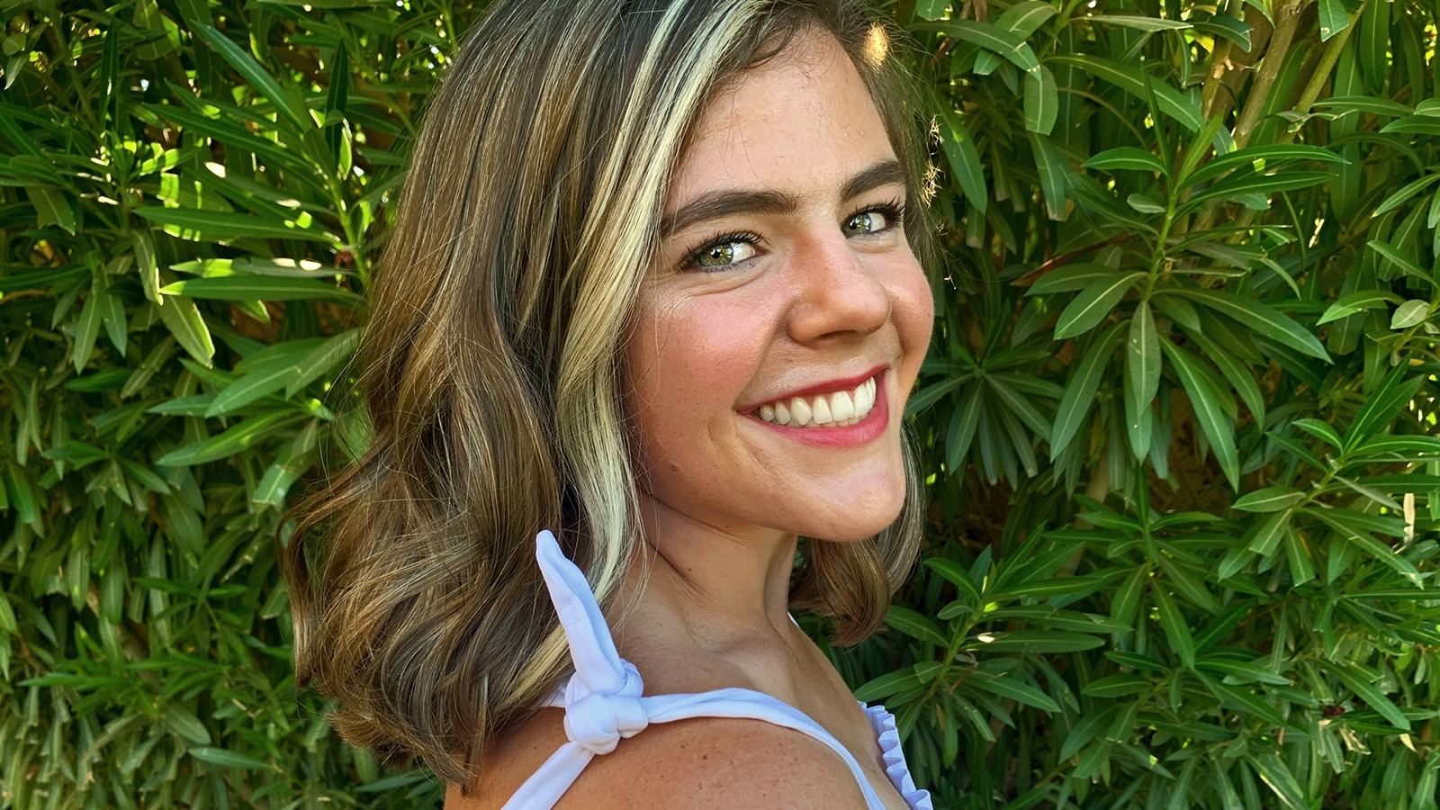 Kathryn Chamberlin poses for an outdoor photo in front of a green hedge.