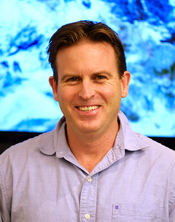 Headshot of Dr. Steven Miller wearing an open collar shirt and standing in front of a satellite image of Earth.