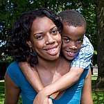 Mom outside with her son on her shoulders. Both are smiling.