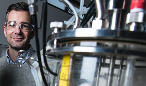 A man stands next to lab equipment containing a microbe.