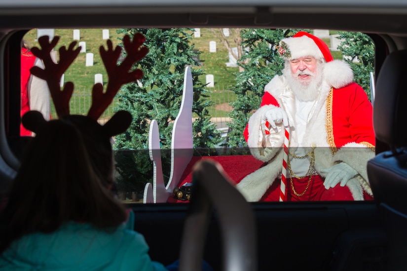 A child in reindeer ears looks out an open car window at Santa.