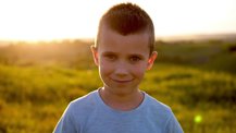 A young boy stands in a sunny field