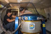 Reseachers Anna Noe and Eric Altman check out the Doppler Aerosol Wind Lidar (DAWN), an airborne instrument that uses pulsed lasers to detect the movement of atmospheric aerosols such as dust or sea salt. In detecting those movements, it can profile wind vector — both speed and direction. Researchers are testing DAWNs capabilities during flights over the eastern Pacific. Credits: NASA/Lauren Hughes