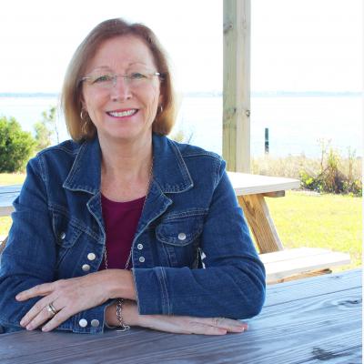 Vanda Lewis sits at a picnic table by a shoreline.