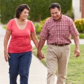 An older couple, holding hands, walking on a sidewalk in a neighborhood.