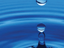 Drop of water after it has hit a body of water with droplets in the air and ripples flowing out from the epicenter.