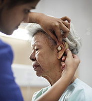 Elderly female patient getting a hearing aid fitted by a medical worker.