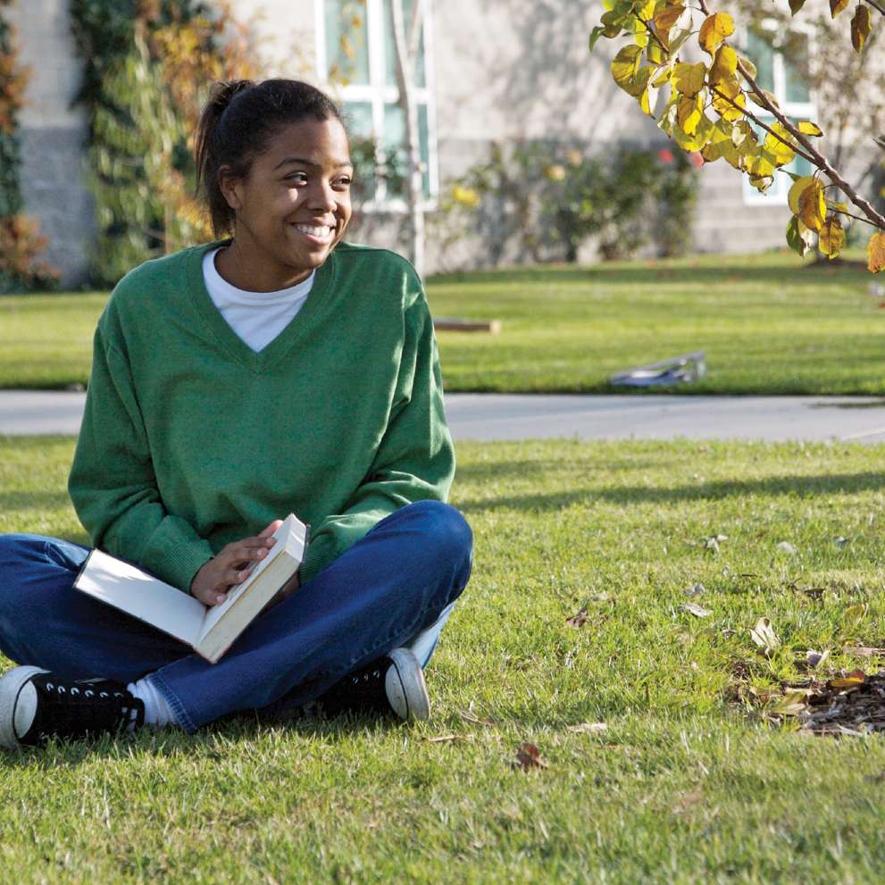 A smiling student studies outdoors on a lawn. 