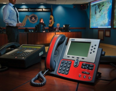 Inside a Strategic Information and Operations Center conference room with two telephones, a large screen, and several people.