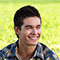 a smiling young man sits on grass in the sun