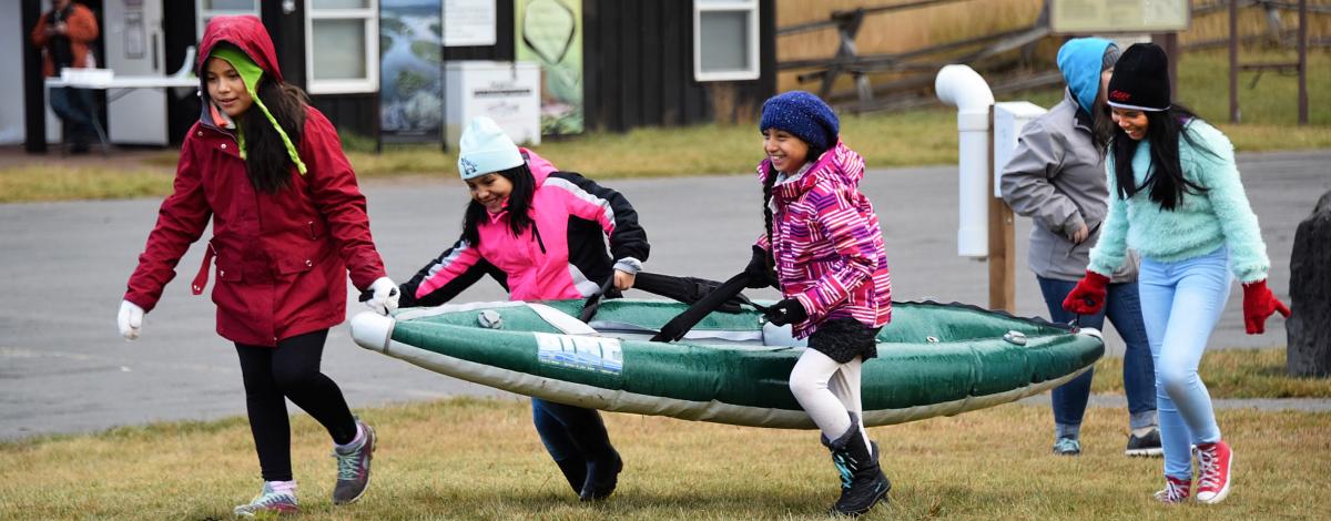 Fourth graders laugh while carrying a kayak at the South Fork of the Snake River in Idaho