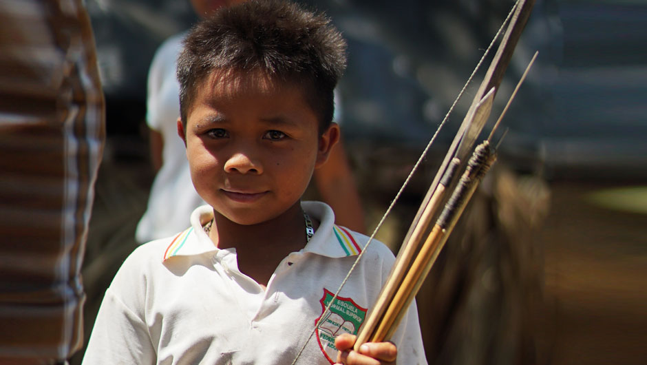 A Colombian toddler smiles at the camera while a group of adults are hard at work behind him.