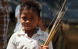 A Colombian toddler smiles at the camera while a group of adults are hard at work behind him.