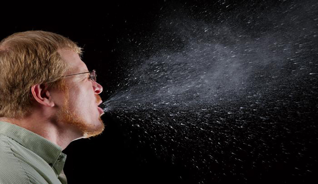 Photo of a sneeze in progress, revealing plume of salivary droplets as being expelled in a large cone-shaped array from man's mouth, thereby, dramatically illustrating the reason one needs to cover his/her mouth when coughing, or sneezing, in order to protect others from germ exposure. | Photo Credit: CDC/Brian Judd