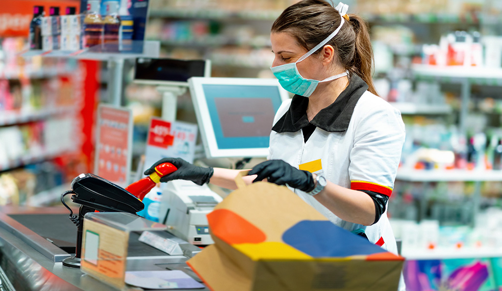 Woman cashier in mask and gloves working at the register | Photo Credit: iStockphoto-1214451229 | Copyright: zoranm