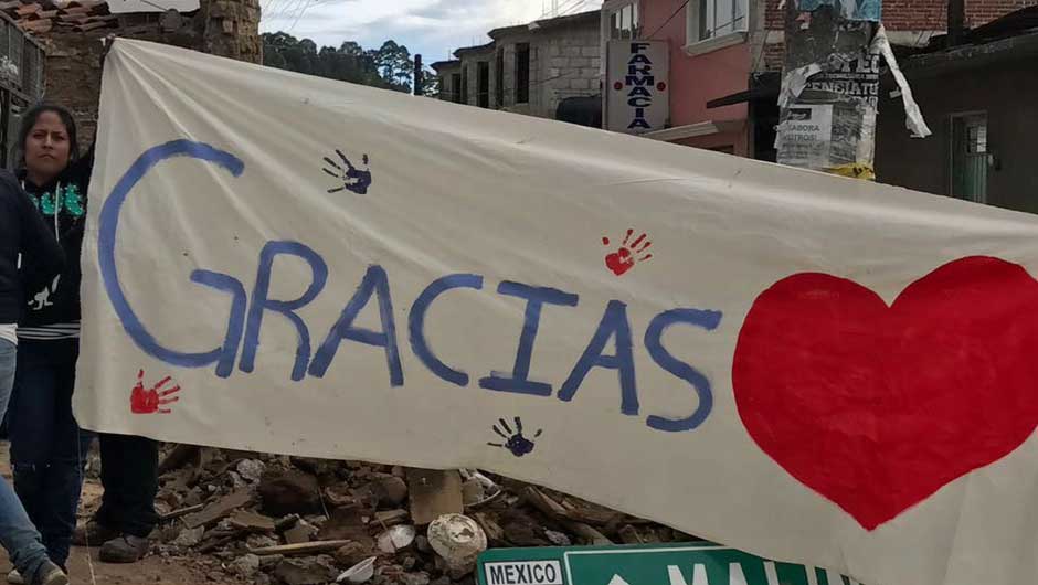 A woman holding up painted sign saying Gracias with a red heart and handprints