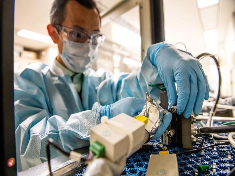 Photo of a researcher dressed in safety equipment and gloves handling machinery