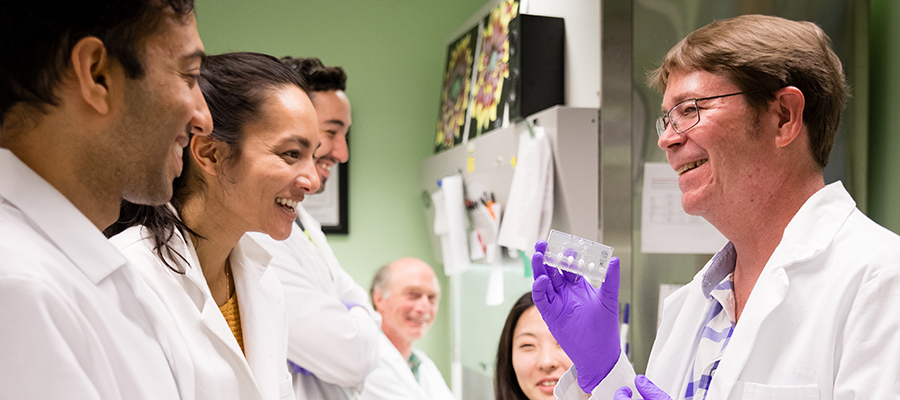 Group of scientists inspect a test unit being held up by a fellow scientist.