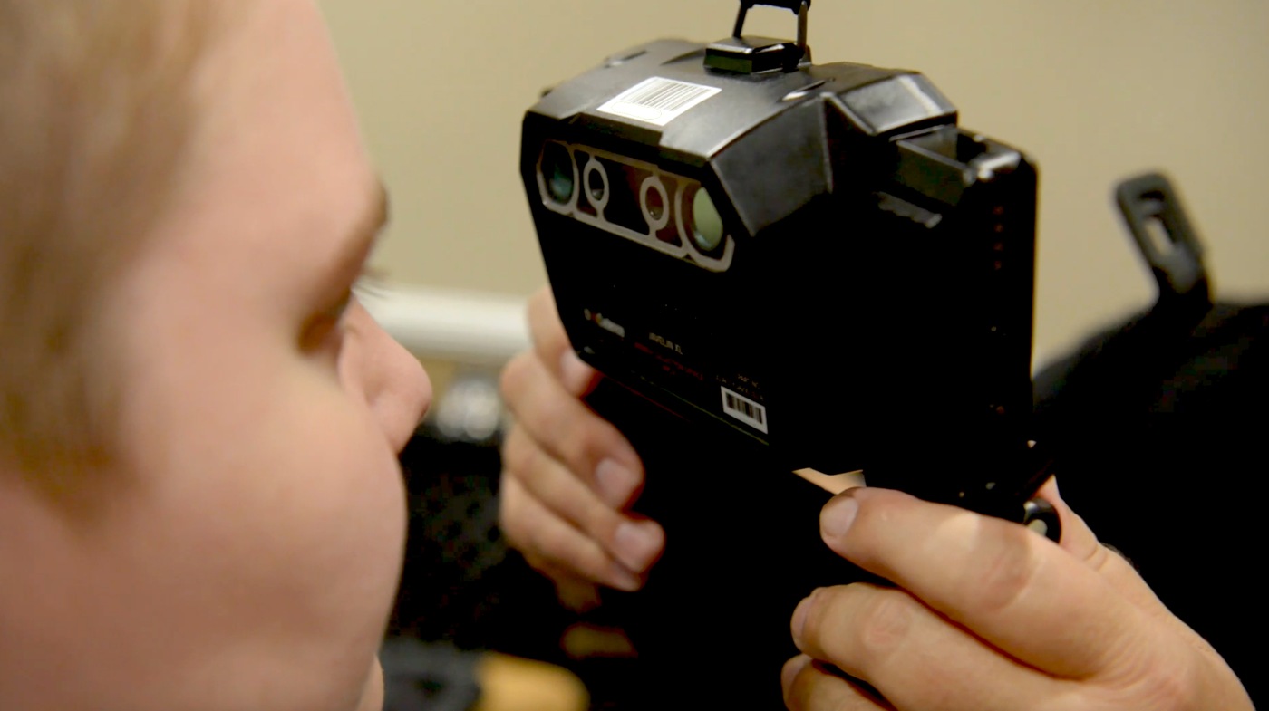 Two people demonstrate how a device is used to capture imagery of irises for the Next Generation Identification (NGI) Iris Service.