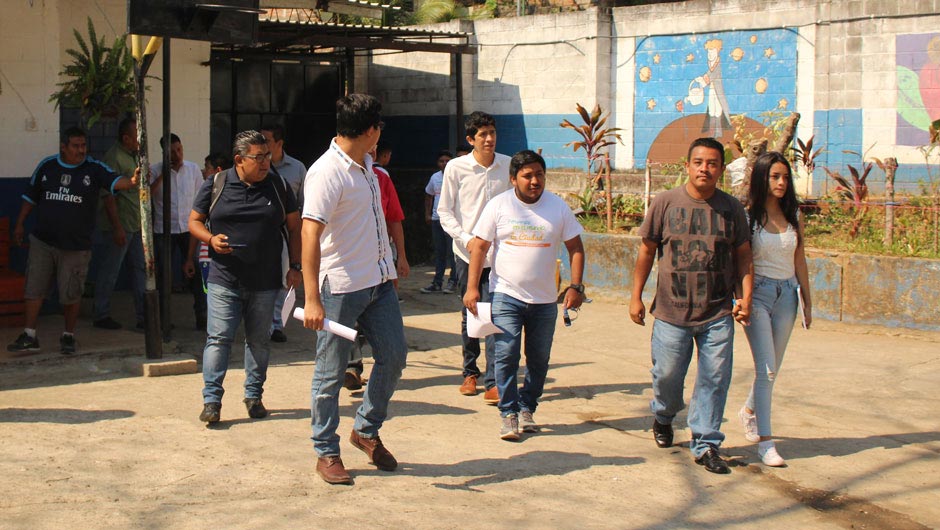 A group of young Salvadorans stream out of a building into the sunshine.