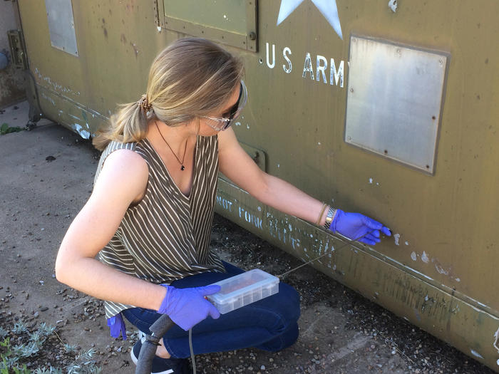 Woman in safety goggles handles an instrument with a thin metal tube at the end.