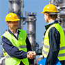 Two men wearing hard hats and bright yellow-green vests shaking hands at a chemical facility.