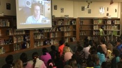 Seated in a school library, third-grade students from Illinois ask National Weather Service forecaster Tim Brice their weather questions via video conference.
