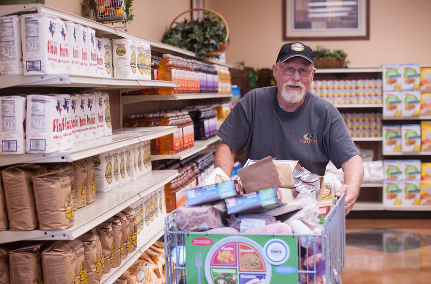 man shopping in a store with a cart full of grocery items