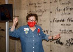 June Robbins points to the Rosies entry in the Labor Hall of Honor while standing by a Rosie the Riveter poster