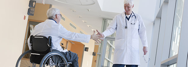 Two doctors shaking hands in hospital corridor, one with spinal cord injury and in a wheelchair