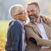 A happy older couple at a park, sitting close together on the ground, and the woman has her arm around the man.