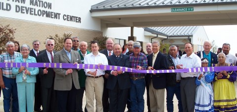 Choctaw Nation opens its child care center in Durant, Okla. Several community leaders pose for a ribbon cutting in front of the new facility.