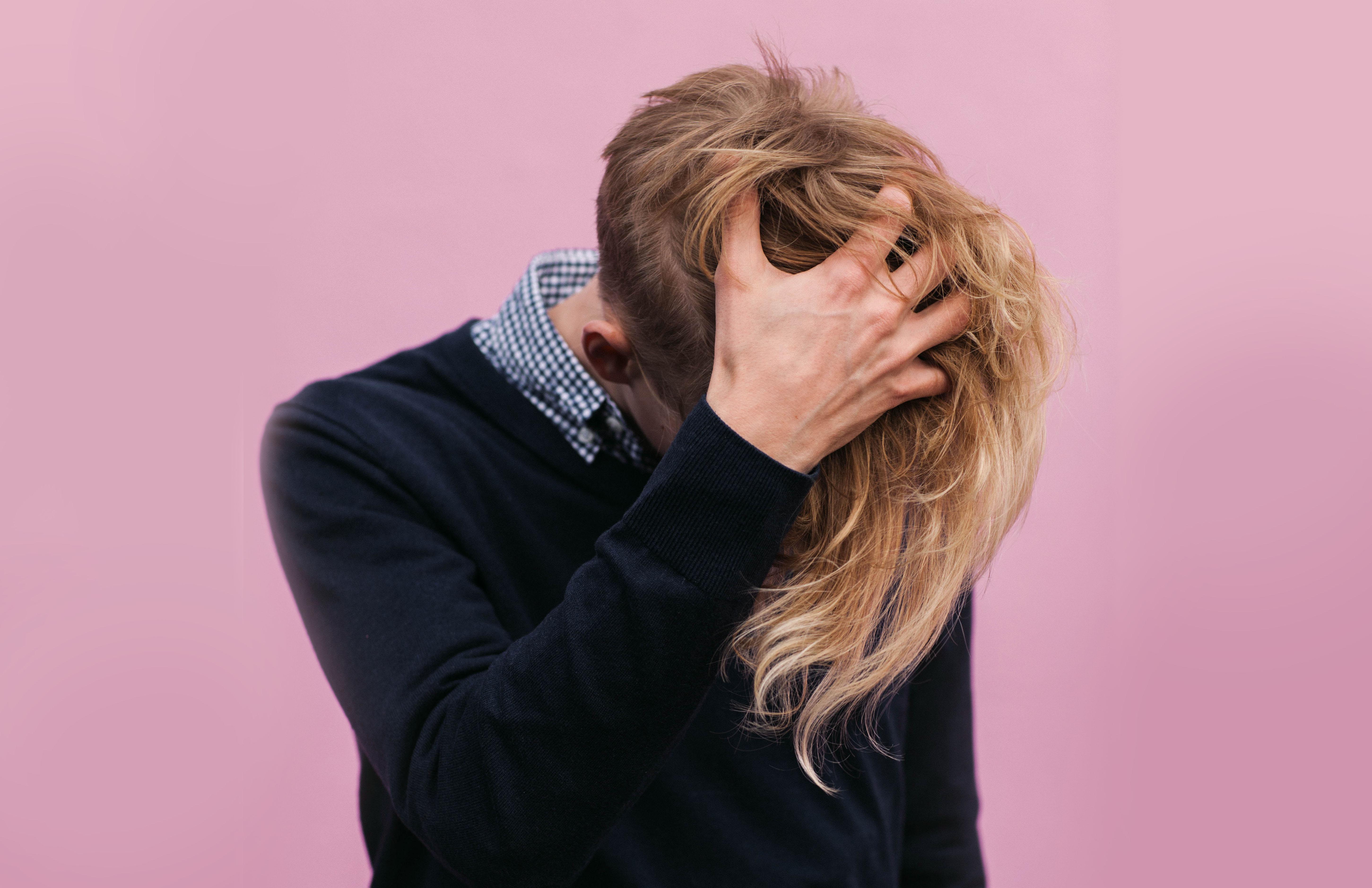 Gender neutral person with long blonde hair on a pink background