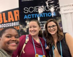 Three people posing in front of a Science Activation booth.