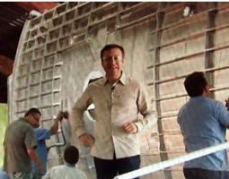 Meteorologist Guillermo Quiroz standing in front of a wooden wall that several men are constructing