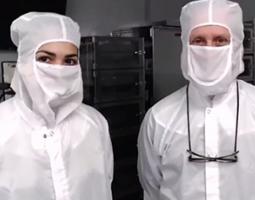 Two scientists posing in white protective clothing and masks. 