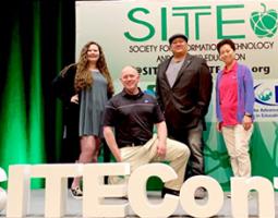 Troy Cline, Carolyn Ng, Lani Sasser, and Eddie Gonzales pose on a state in front of a SITE banner.