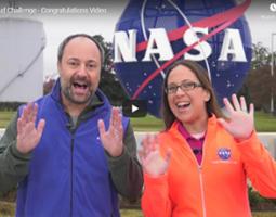 A man and woman holding their hands up in front of the NASA Langley meatball sculpture