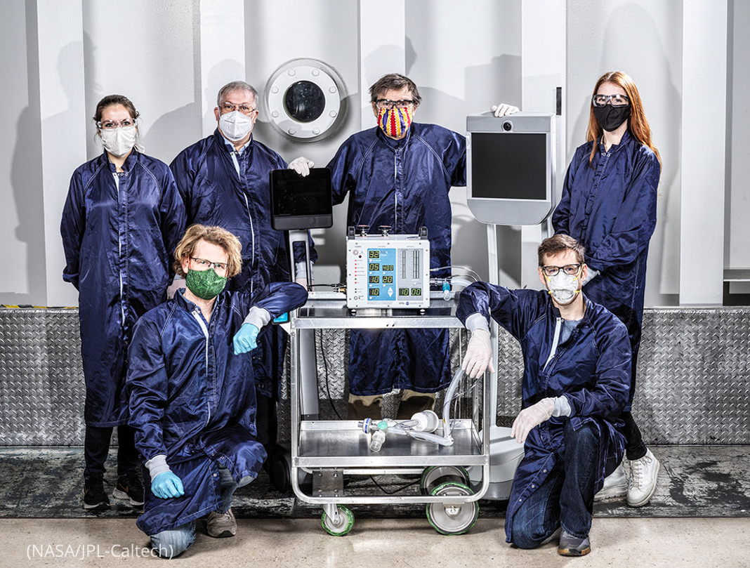 People in protective gear posing with a ventilator prototype (NASA/JPL-Caltech)