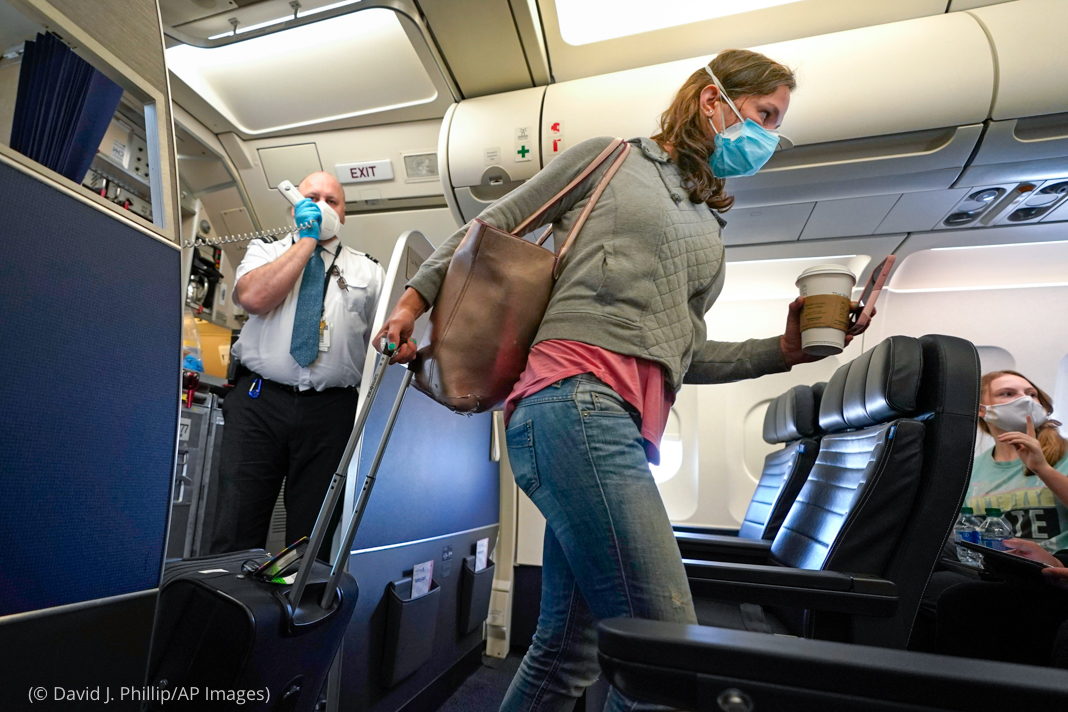 Person wearing mask and walking down aircraft aisle (© David J. Phillip/AP Images)