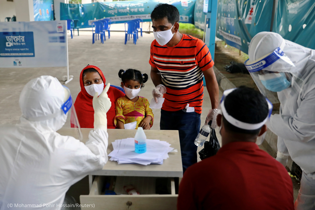 People in face masks across table from others in heavy protective gear (© Mohammad Ponir Hossain/Reuters)