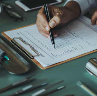 Closeup of a clipboard form on a desk and the hand of a person filling it out with a pen