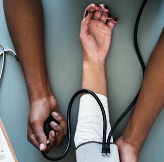 Closeup of an individual getting their blood pressure taken, showing only the arms of the nurse and patient