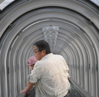 Man standing in an arched hallway holding a baby in front of him, facing away from the camera