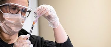 Masked health care worker prepares syringe.