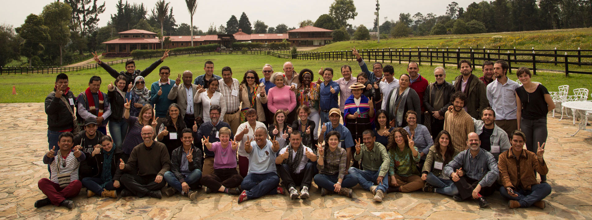 Group of IAF staff and grantee parters smiling and giving peace signs in front of green field with building in the background