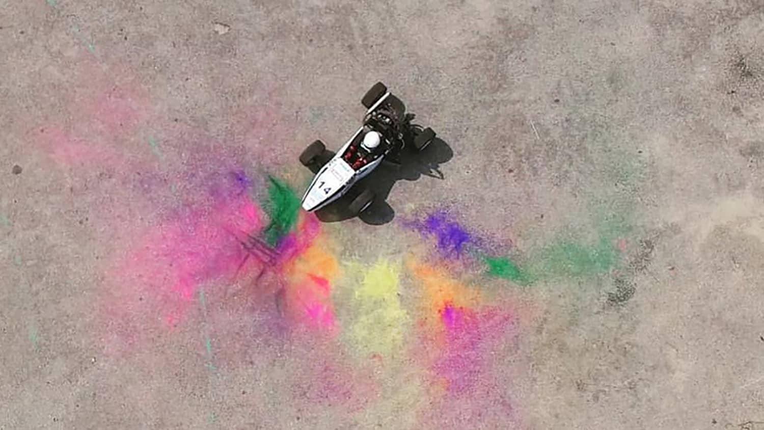 A race car from above, surrounded by bright colored paint or chalk.