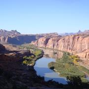 A huge canyon surrounded by deep-set cliffs opens to reveal a sunny gorge and part of the Colorado River.