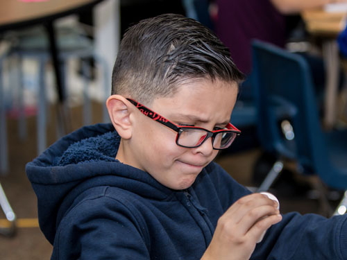 young boy with glasses and blue hoodie scrunching his face while looking at a vial in his right hand