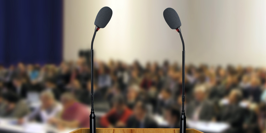 close up of two microphones on podium with people blurred in background